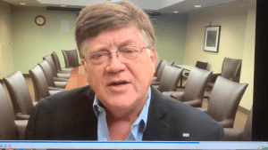 Jim Pancero talking to the camera in a meeting room with chairs behind him.
