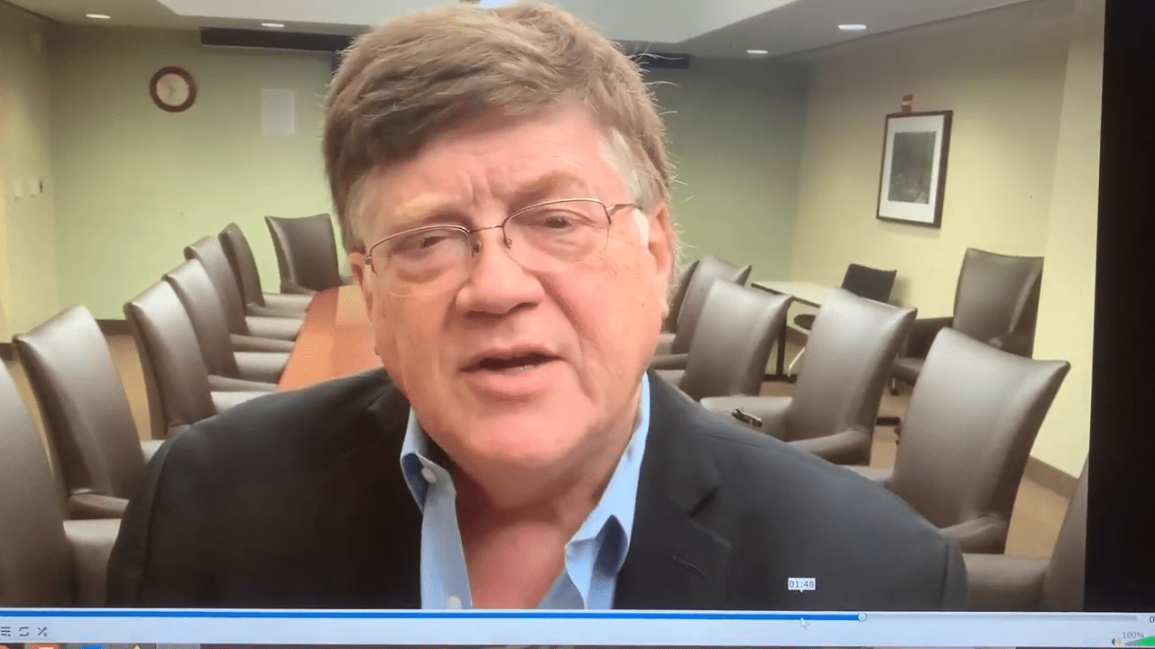 Jim Pancero talking to the camera in a meeting room with chairs behind him.